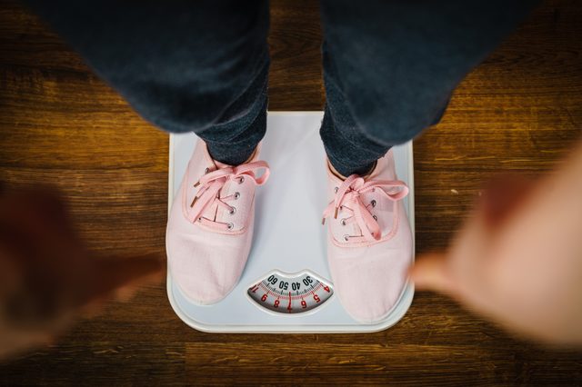 Top view of woman feet wearing pink sneakers on bathroom weight scale. Fit, dieting, fat loss concept.