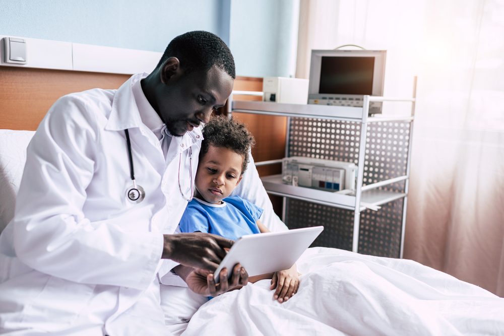 african american doctor and little boy using tablet together in hospital