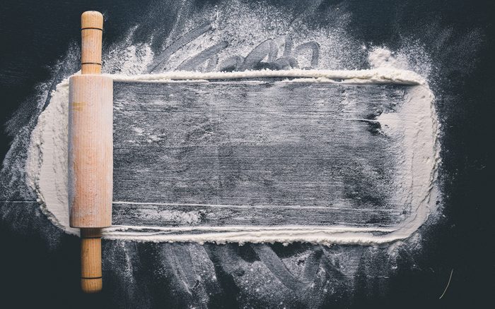 Rolling pin and white flour on a dark background.