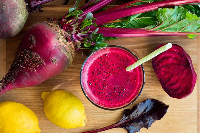 Red beet juice in a glass on a wooden table with whole beets and lemons, top view