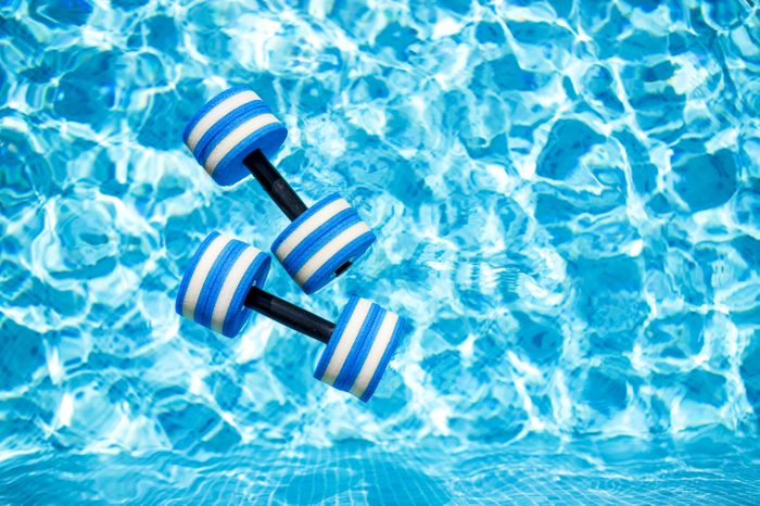 Top view of plastic dumbbells for aqua aerobics floating in blue water of swimming pool on summer day outdoors