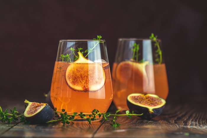 Pink cocktail with fig, thyme and ice in glass on dark wooden background, close up. Summer drinks and alcoholic cocktails. Alcoholic or detox cocktail