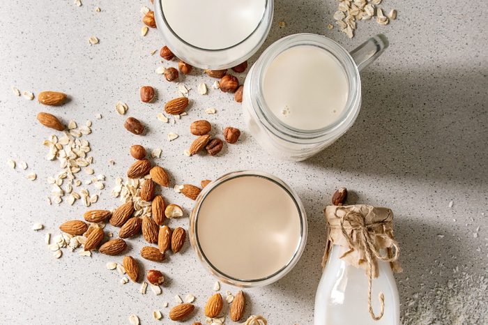 Variety of non-dairy vegan lactose free nuts and grain milk almond, hazelnut, coconut, rice, oat in glass bottles with ingredients above over white spotted background. Flat lay, space
