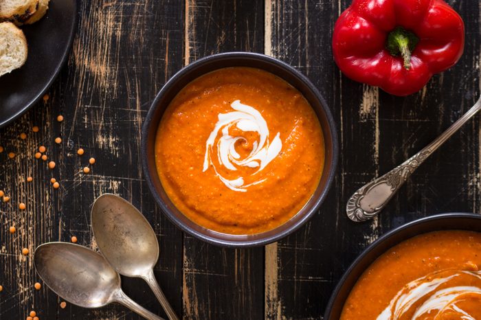 Delicious pumpkin soup with heavy cream on dark rustic wooden table with red bell pepper, bread toasts, lentil. Top view