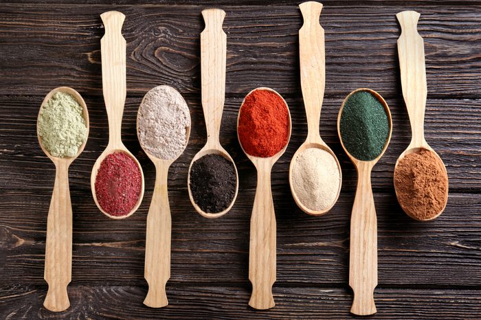 Different colorful superfood powders in spoons on wooden table