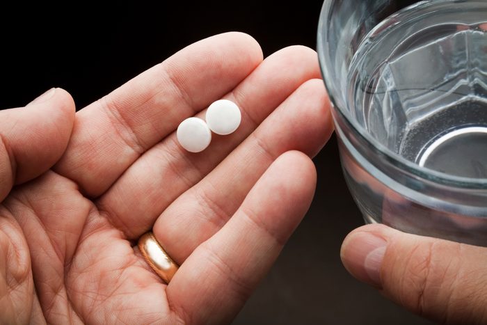 hands holding two pills and glass of water