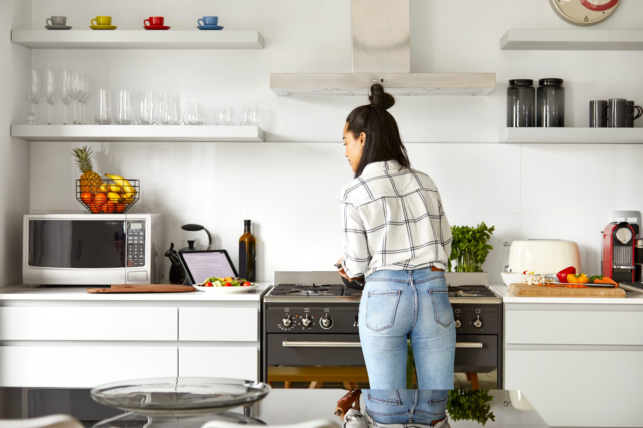 Woman cooking food while looking at digital tablet