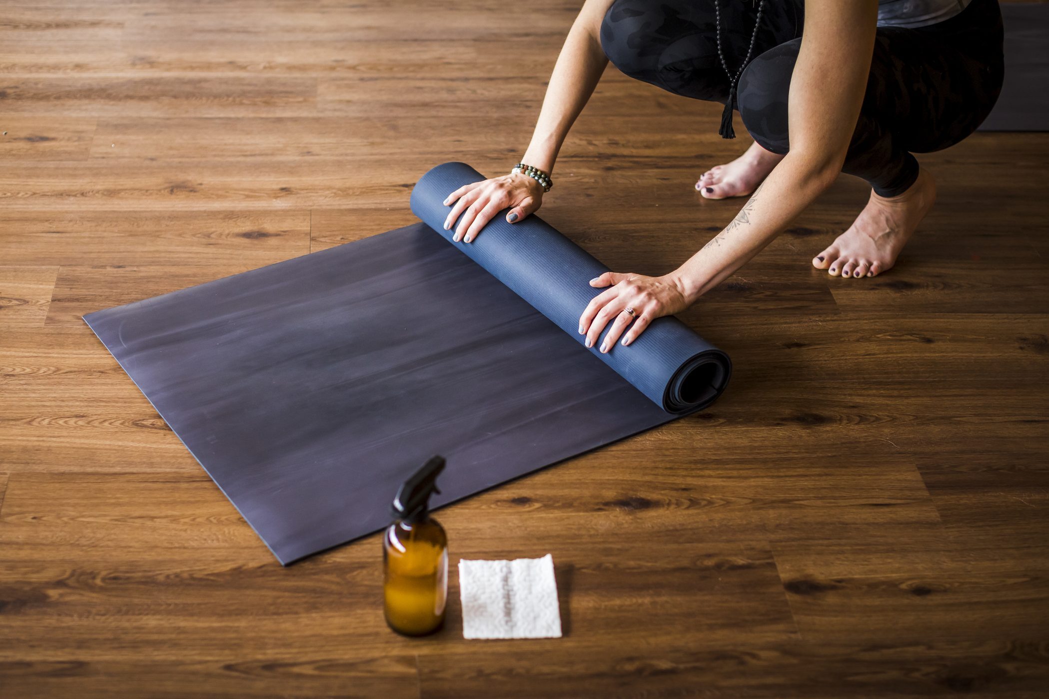 Woman rolling up yoga mat with sanitizer nearby.