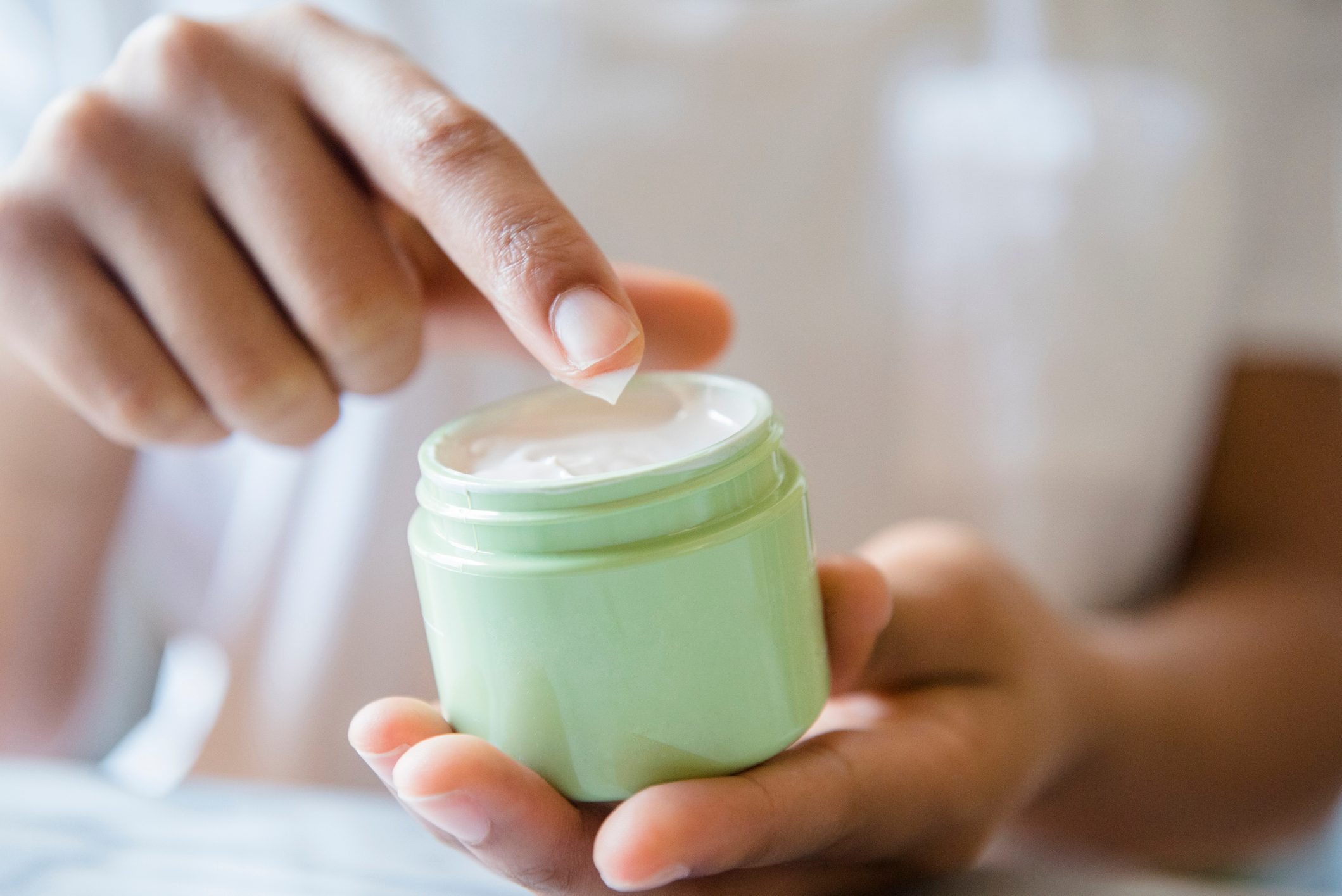 Close up of African American woman dipping finger in lotion jar