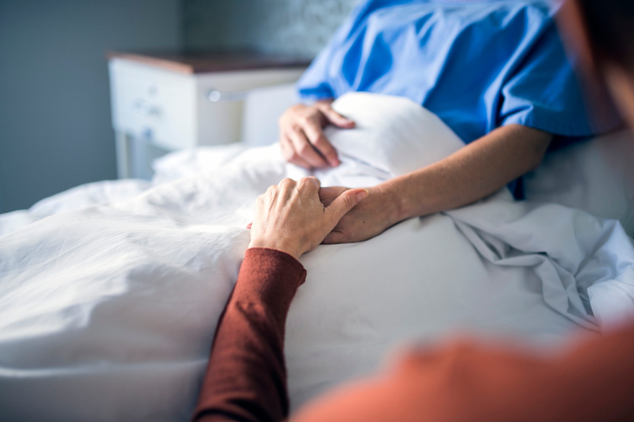 Woman holding hand of sister in hospital bed