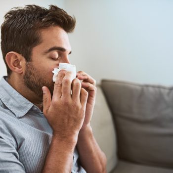 close up of young man blowing his nose while sitting on couch at home
