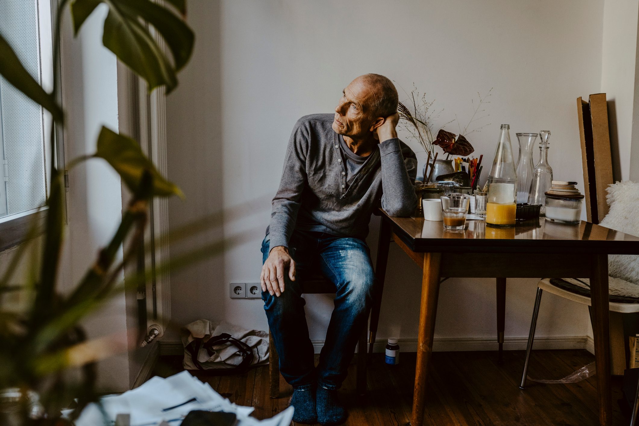 worried senior man sitting on chair in living room and looking out the window