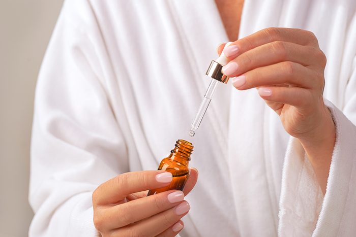 Woman in white bathrobe holds Beauty Product Facial Serum.