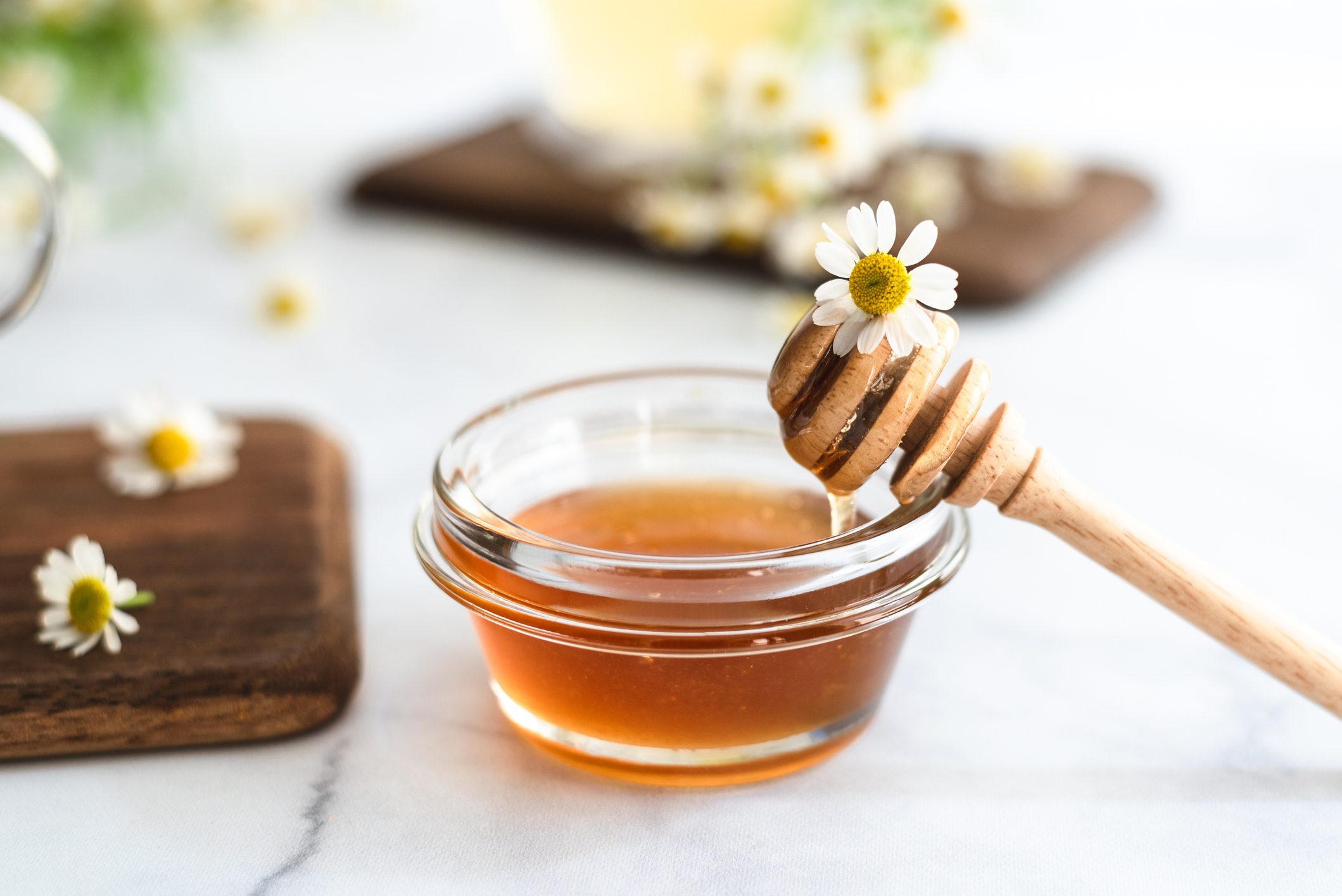 Close up to glass container with honey and chamomile flowers