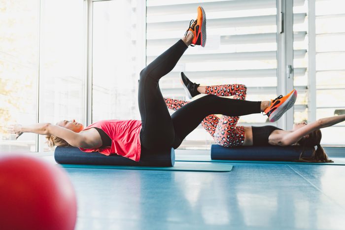 two women doing dead bug exercises on yoga mats in a gym