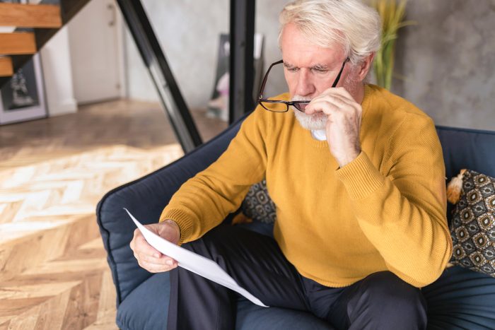 Senior man reads document from bank about credit debt. Financial crisis concept.