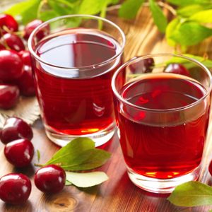 Cherry juice with fresh berries and leaves on a wooden background