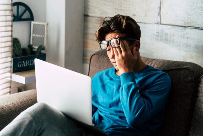 Stressed student at home studying with personal laptop computer - tired teenager for school work -internet. addiction for game or job search concept - indoor technology activity