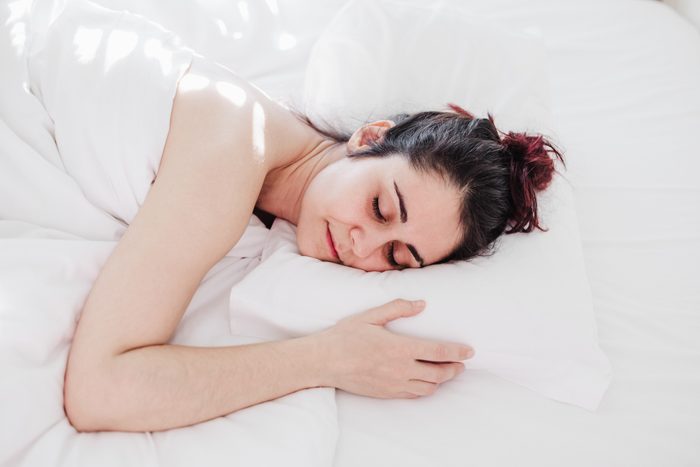 Top view of attractive young woman sleeping well in bed hugging soft white pillow. girl resting, good night sleep concept. Lady enjoys fresh soft bedding linen and mattress in bedroom