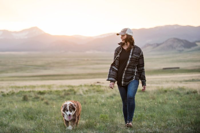 woman walking dog in a field with mountains in the background during sunset
