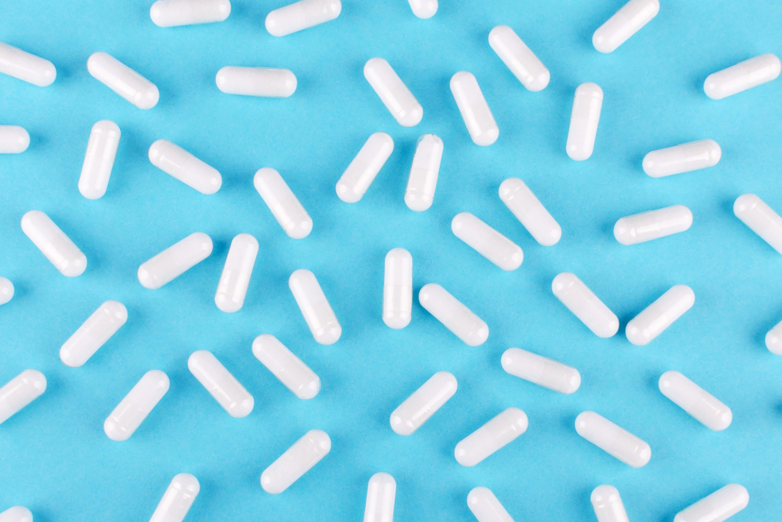 white medicine capsules on blue background, view from above