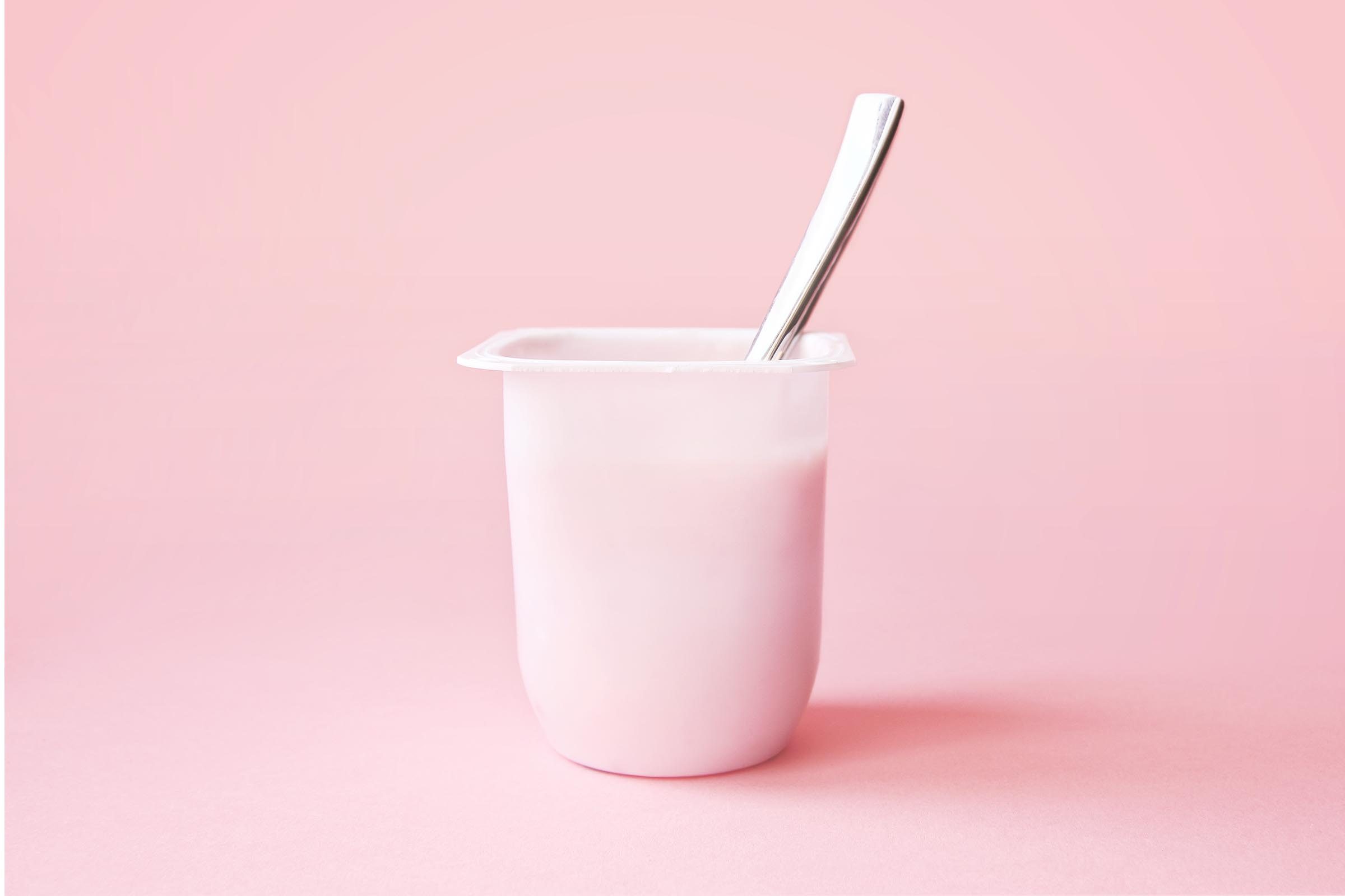 yogurt in a plastic cup with spoon on a pink background