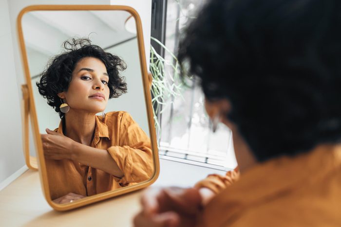 A Beautiful Natural Woman Looking At Her Face In The Mirror And Checking Her Make Up