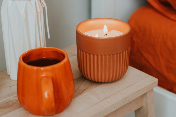 Wooden nightstand with candlelight flame, vase with dry flowers and tea mug. Autumn cozy mood concept. Cute autumn hygge home decor arrangement.