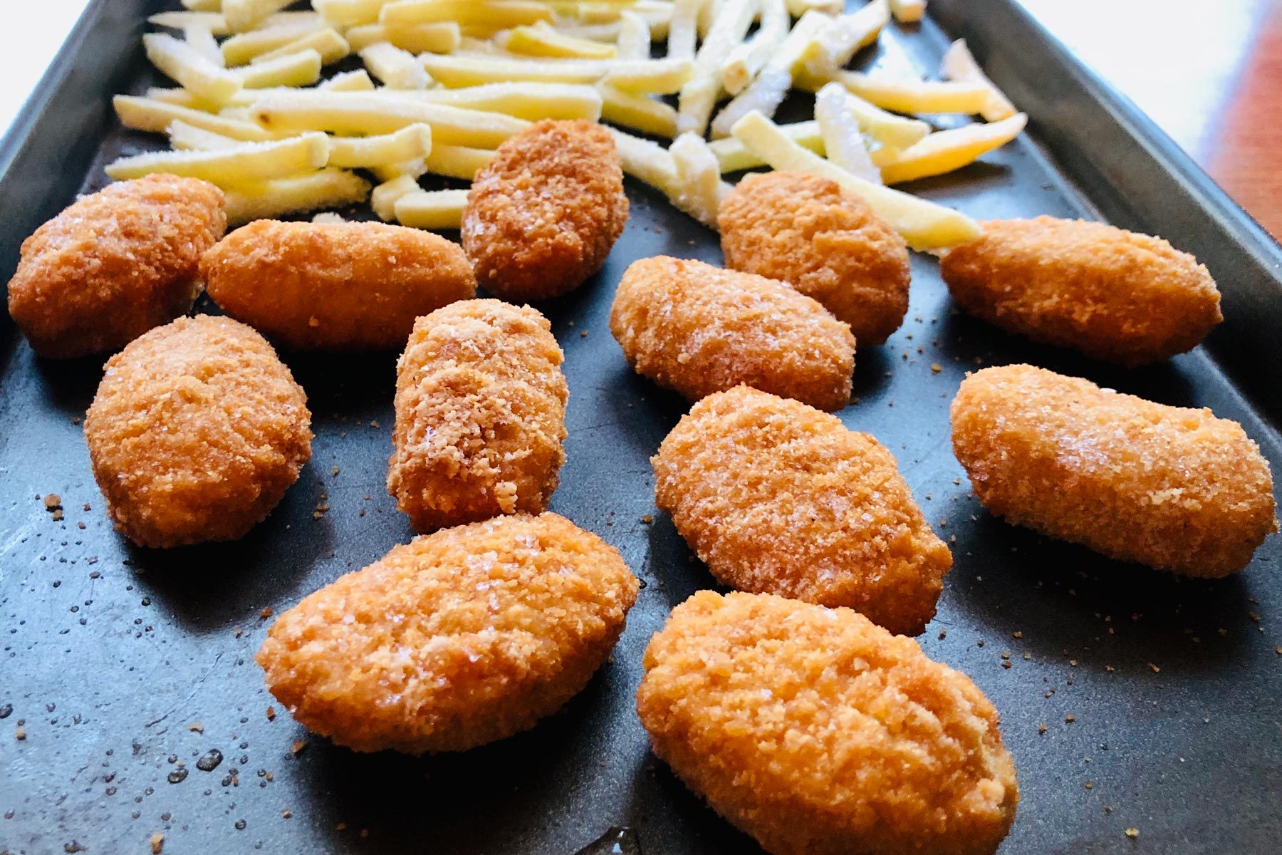 Frozen chicken nuggets and French fries on baking pan