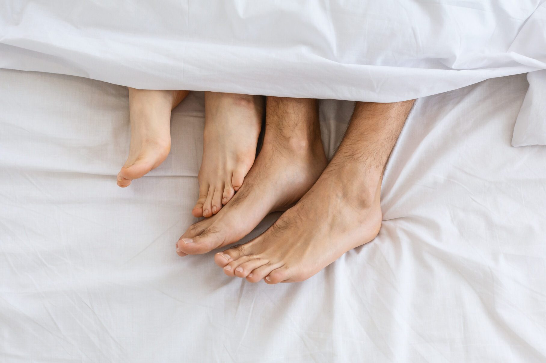 Loving couple in bed. Female legs stroking male legs