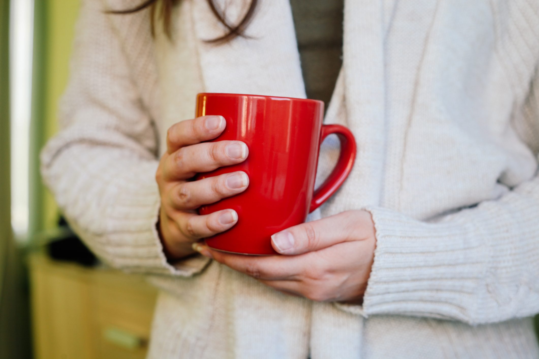 Woman holding red cup of hot drink at home.