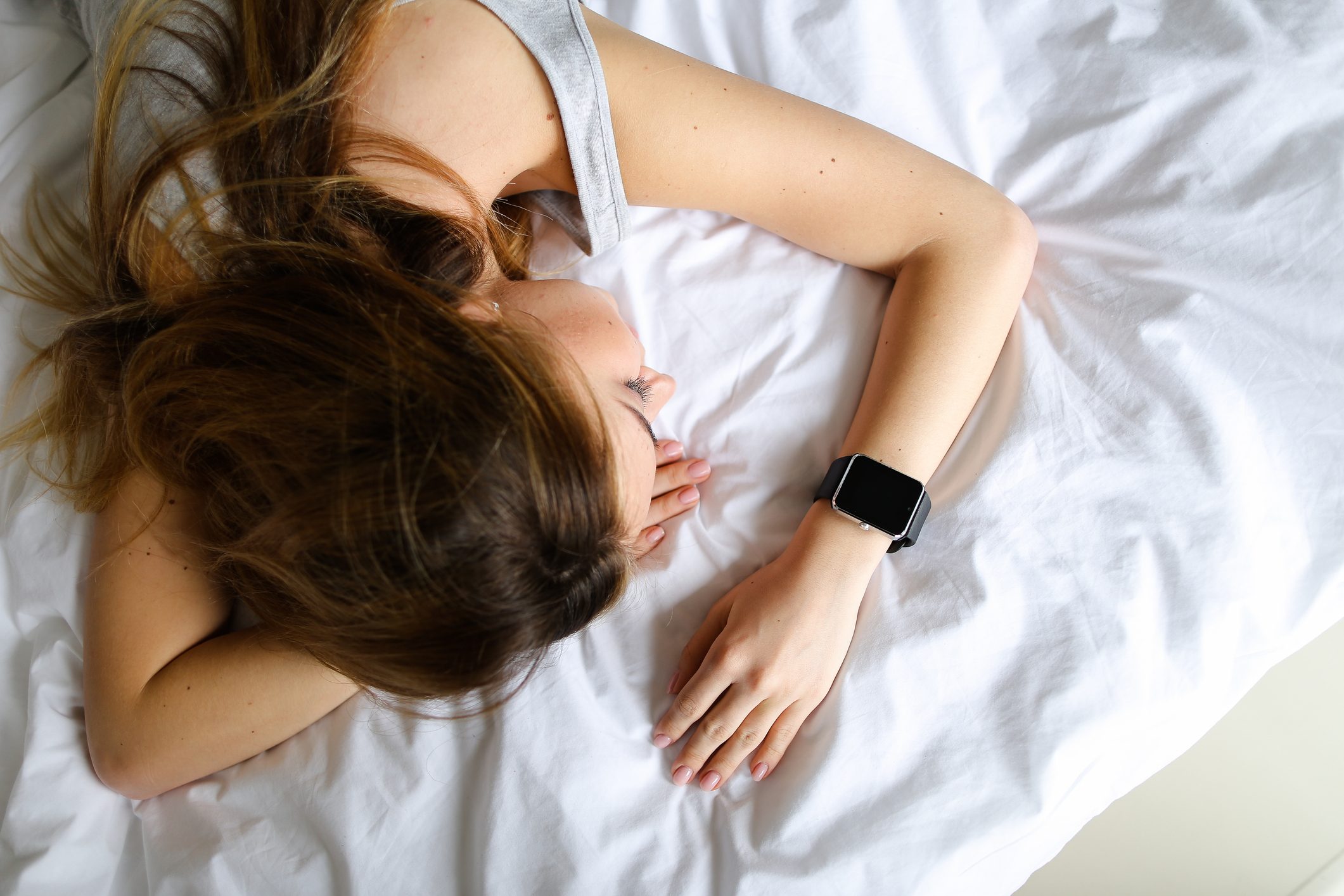 Young european girl lying on bed with smart watch, white linens background