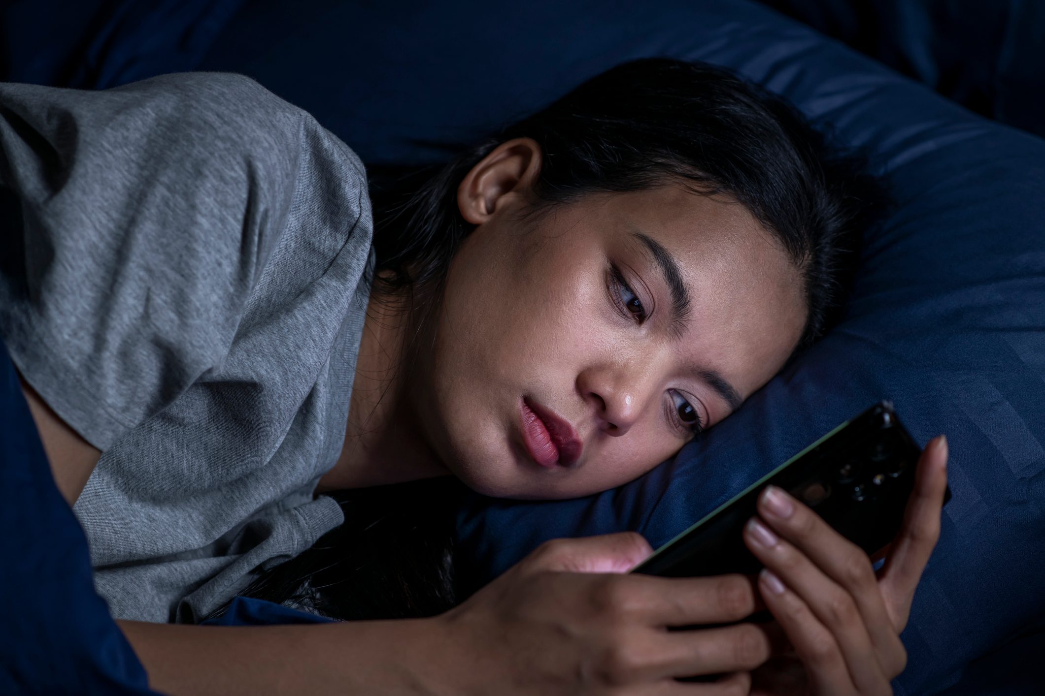 Exhausted young Asian woman using smartphone late at night.