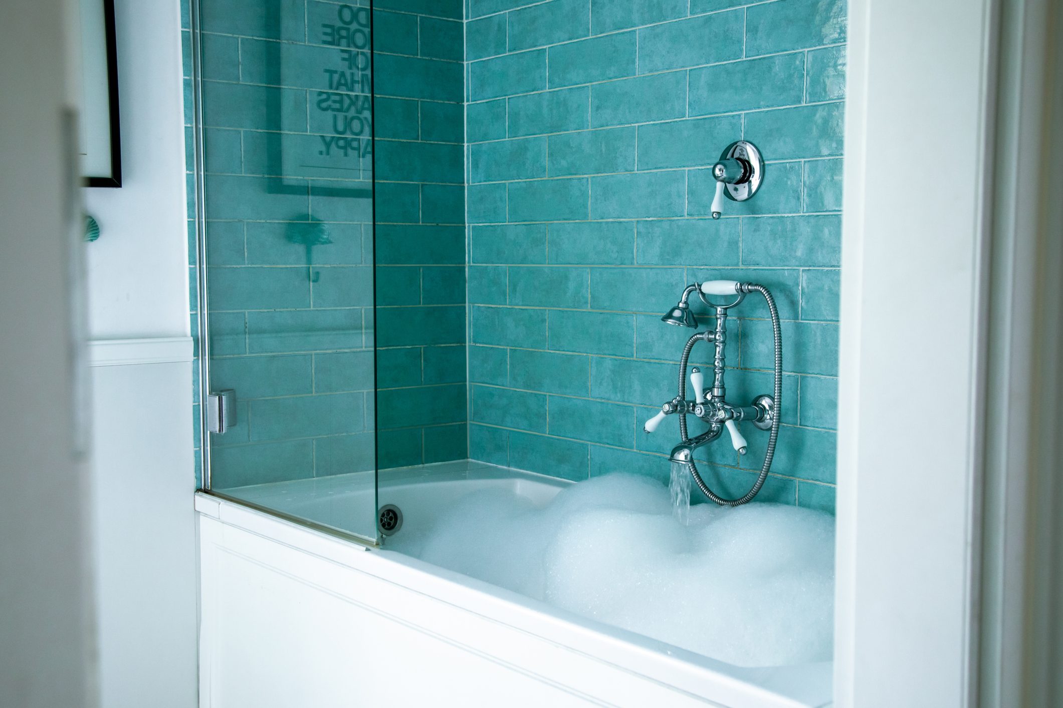Photo of stylish bathroom with white bathtub being filled with hot running water and soap foam