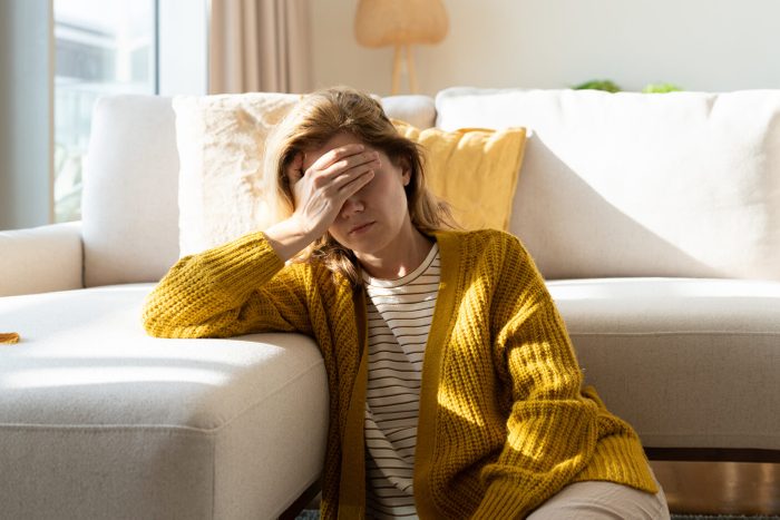 Woman having headache and holding her head while sitting on the floor at home
