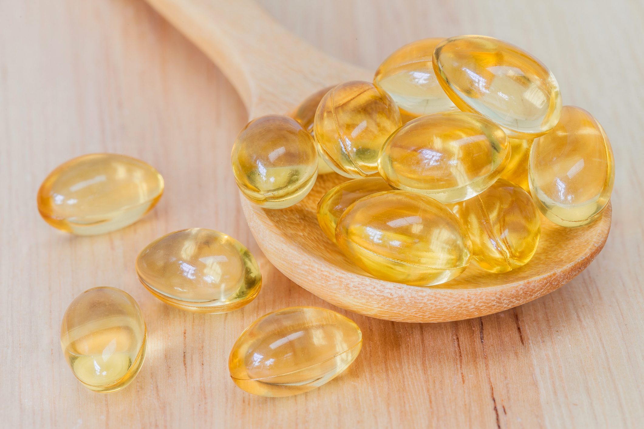 Fish oil supplement capsule on wooden spoon and wooden background
