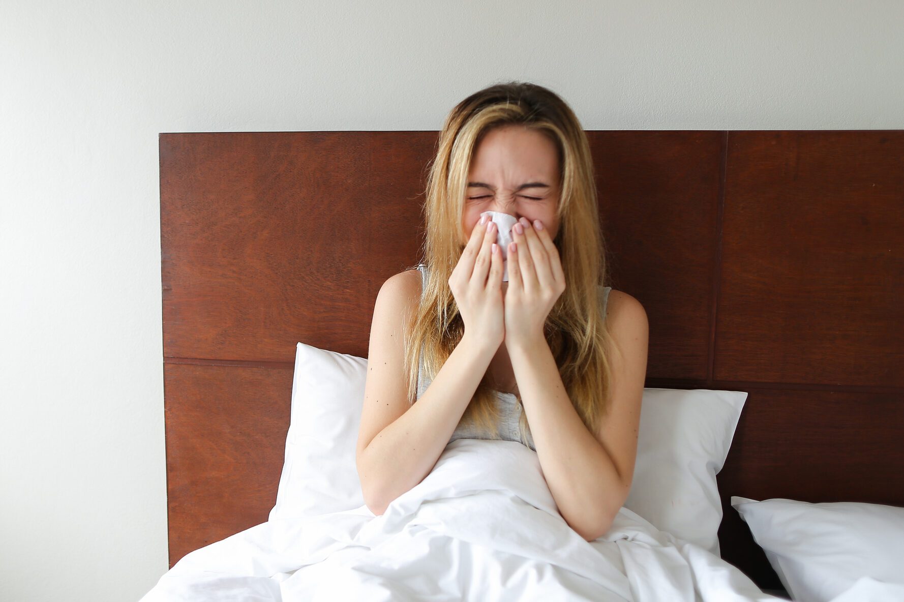 Young woman siitng on bed with running nose and tissues