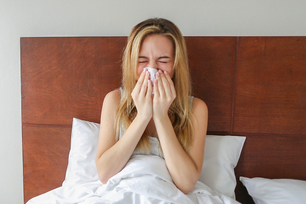 woman sitting on bed with running nose and tissues