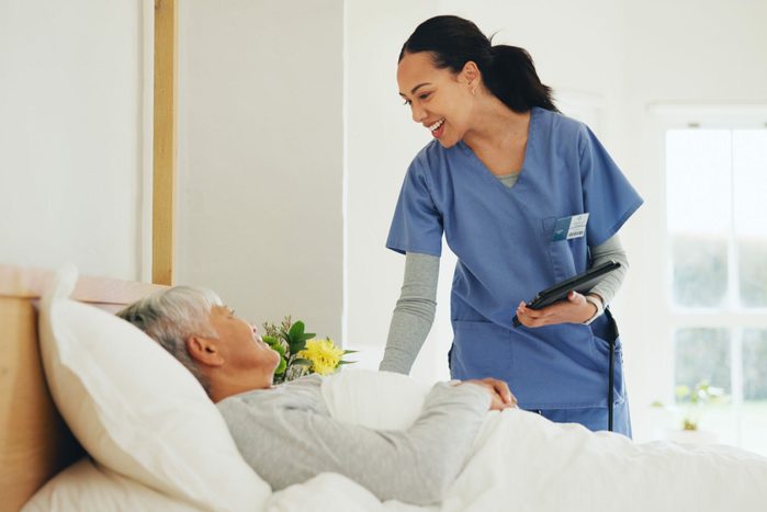 Happy woman, nurse and tablet with patient in bed, elderly care or checkup at old age home. Female person, doctor or medical caregiver smile with technology and client lying in bedroom for healthcare