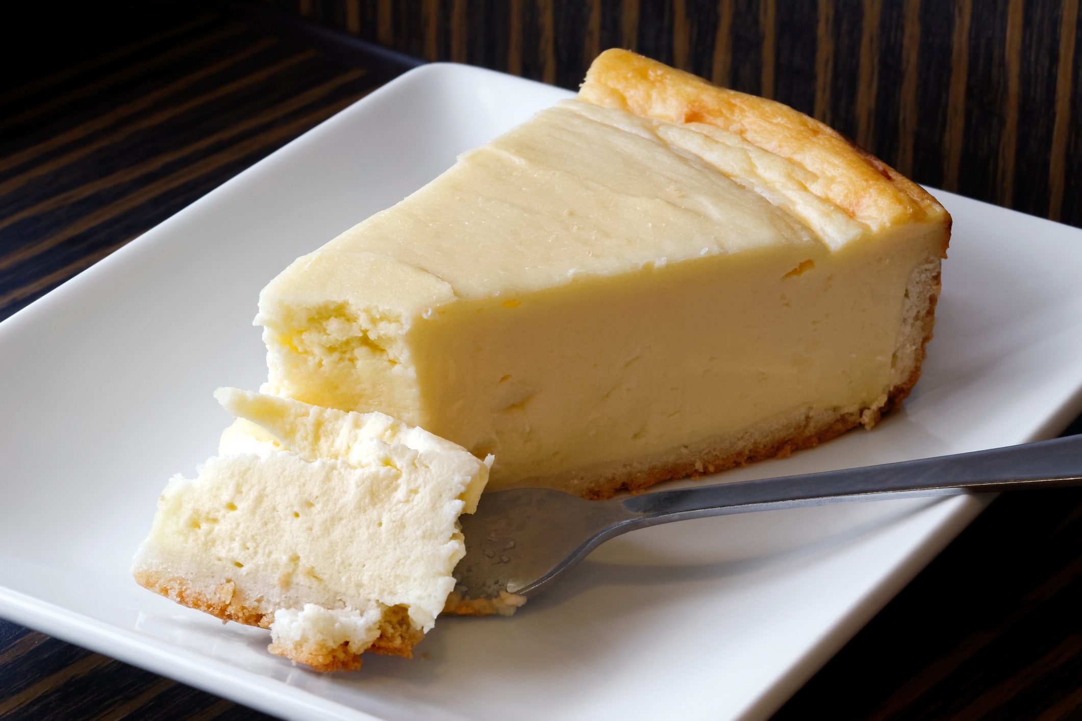 Plain Baked Cheesecake With Cake On Fork On White Ceramic Plate. Brown Background.