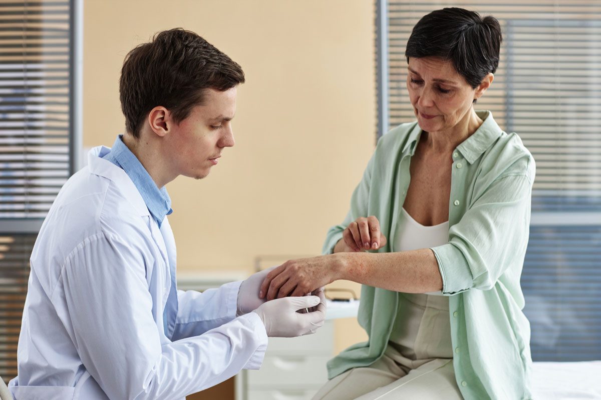 doctor examining hands of mature woman during consultation in dermatology clinic