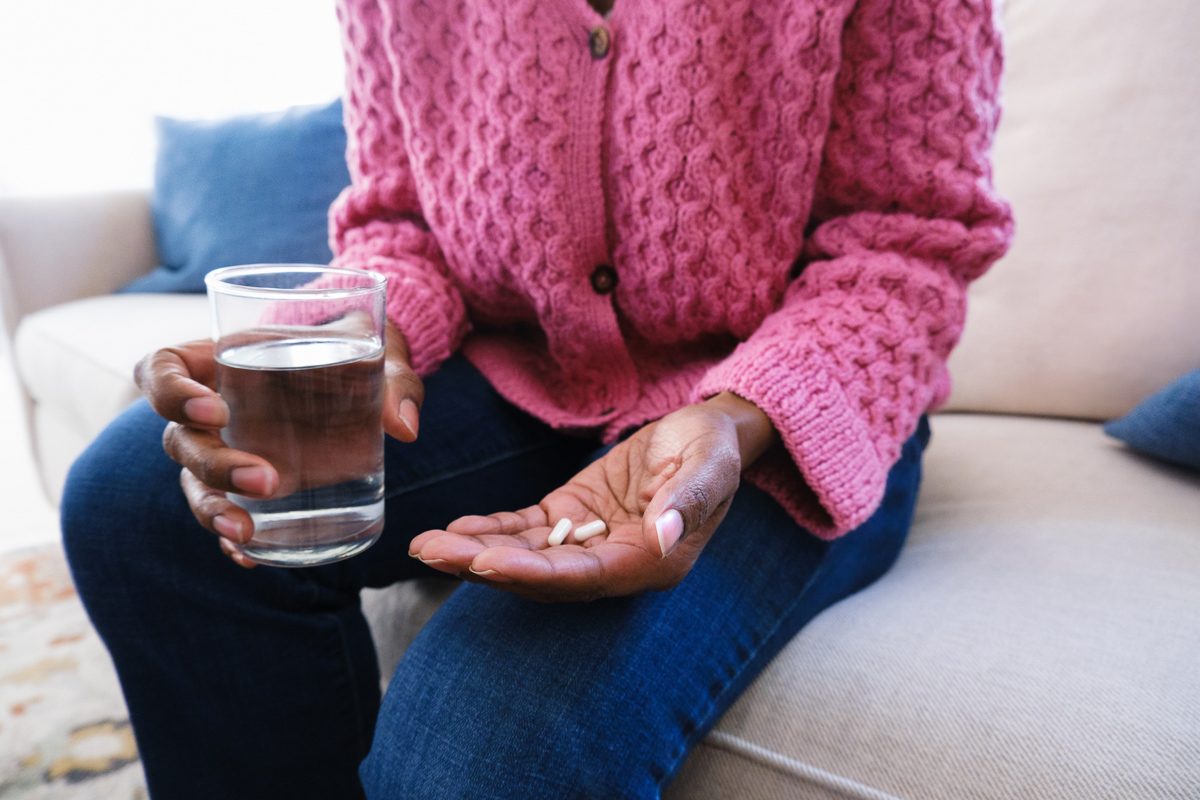 woman holding glass of water and capsules