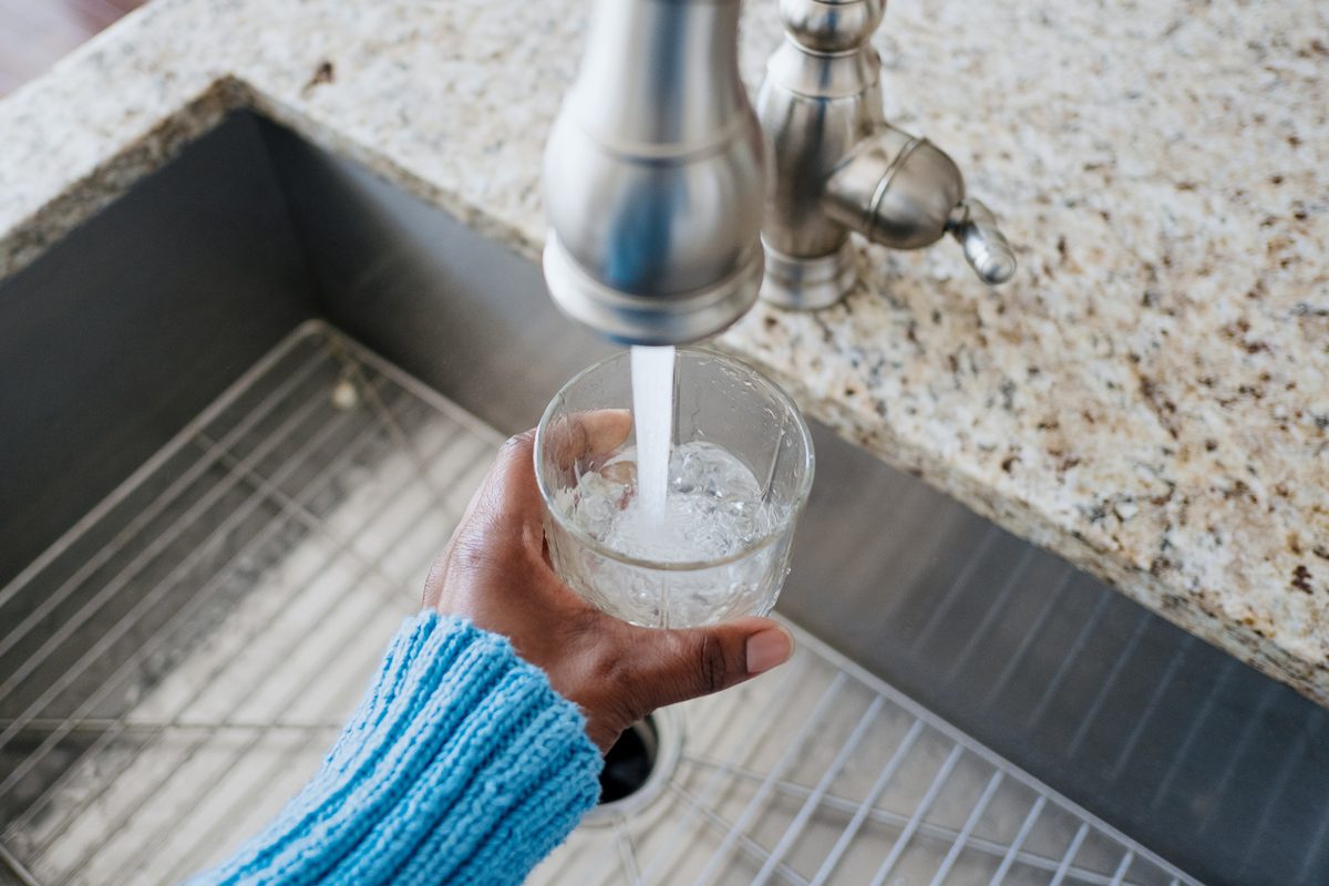 woman pouring water in glass from tap