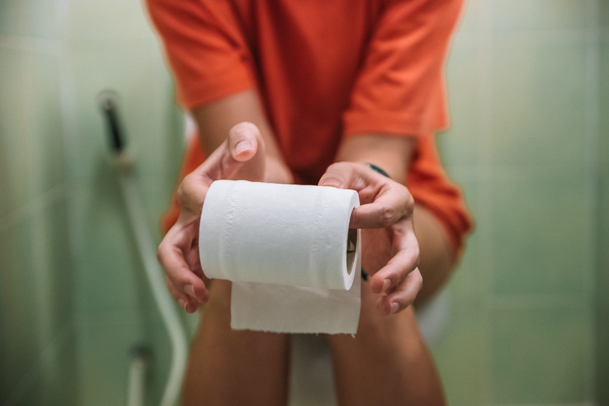 person sitting on toilet holding roll of toilet paper