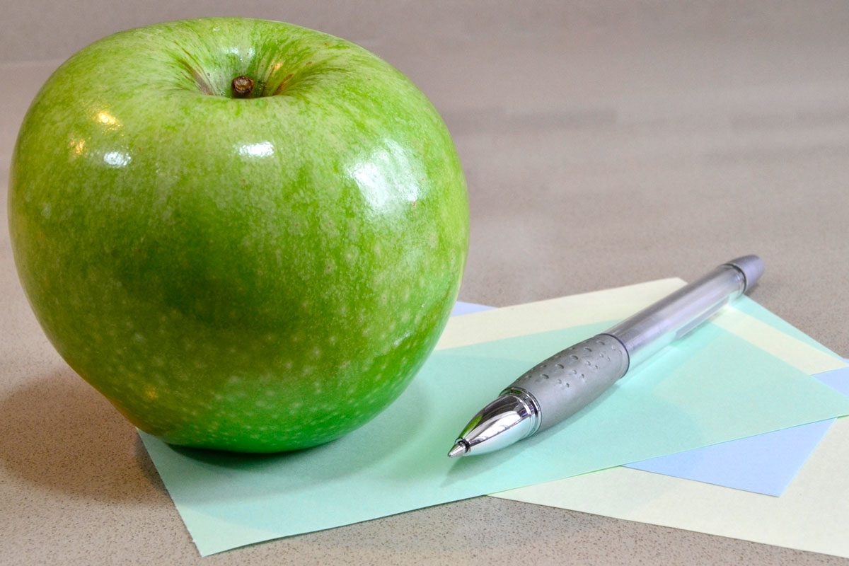 Green Apple And Pen On Color Papers On A Table