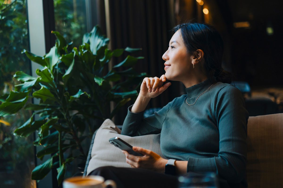 Woman With Smartphone Looking Out Through Window While Sitting In A Cafe